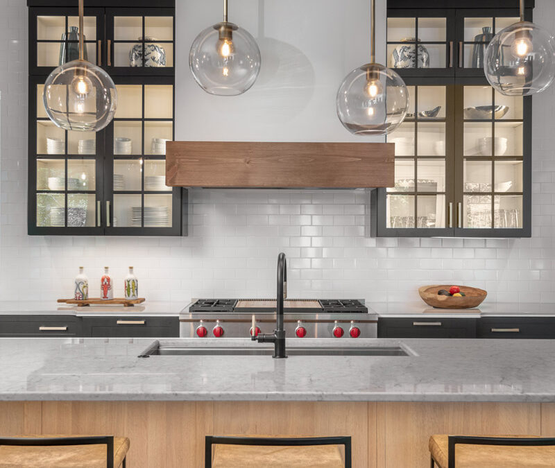 Luxury kitchen island with decorative lighting, wood hood, gas range, and glass cabinetry.
